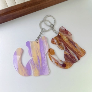 Cat-shaped acrylic keychains with colorful marble texture and metal rings on a tray