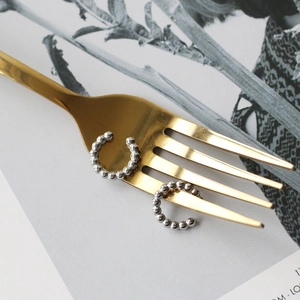 Close-up of polished silver beaded ear cuffs hanging on a gold fork for stylish detail