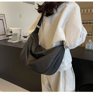 Close-up of a large black Oxford cloth hobo bag worn by a model in a cafe setting