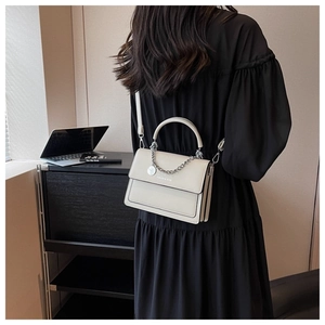 Modern white handbag with metal chain and top handle shown on a model for scale