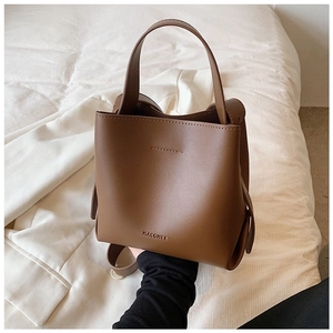 Close-up of brown leather bucket bag with top handle and embossed logo on white fabric