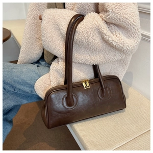 Detailed macro of dark brown leather cylindrical baguette bag with gold metal zipper closure