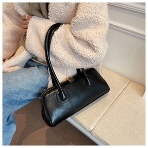Detail of a chic black PU leather handbag with gold zippers held by a model in a beige coat