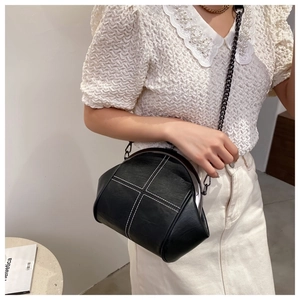 Detail of black frame bag with white cross stitching and metal chain strap on model