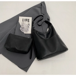 Detail shot of the black leather bucket bag and matching pouch on a gray blazer