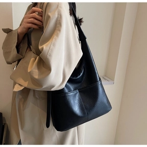 Detail of a black large capacity leather bucket bag worn with a classic khaki trench coat