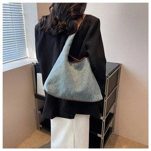 Detailed view of light blue denim tote bag with brown leather straps worn on shoulder