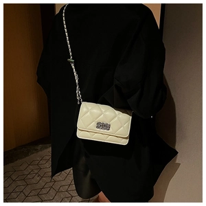 Detail of cream quilted crossbody bag featuring silver chain strap and metal lock closure
