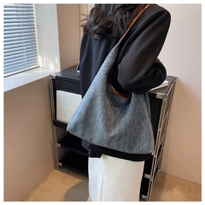 Detail view of large denim tote bag with brown trim carried by model in professional setting