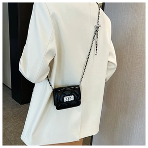 Close-up of black quilted chain bag worn over a beige blazer with silver turn-lock detail
