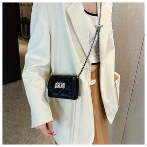 Close-up of black quilted mini square bag with silver chain strap worn by a model