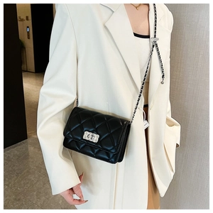 Detail of black quilted chain bag with silver lock worn on white blazer jacket