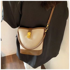 Detail showing brown and beige canvas bucket bag with gold hardware on a model