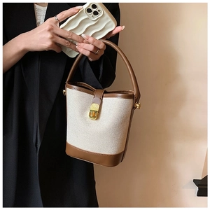Detail of canvas bucket bag with brown leather trim and golden metal lock closure