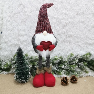Christmas gnome doll with heart and long red knit hat on snowy festive background