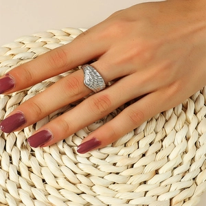 Detailed view of silver angel wing ring with feather texture on a woven background