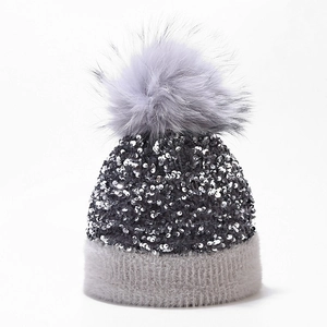 Close-up of sparkling silver sequins and a fluffy grey faux fur pompom on a winter knit beanie