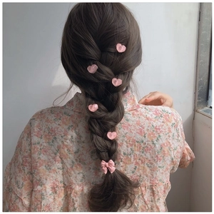 Detail of pink bow and heart hair clips styled in a braided ponytail hairstyle