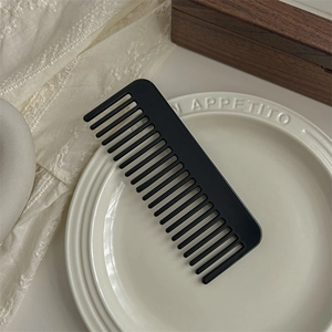 Close-up of black matte wide-tooth comb for hair styling on an elegant ceramic plate