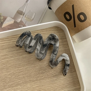 Macro detail of wave-shaped acetate hair claw clip with marble texture on wooden tray