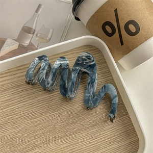 Macro view of wave-shaped acetic acid hair claw clip with blue marble ink texture