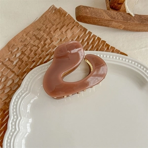 Macro view of caramel-colored acetate claw clip with gold spring on a ceramic plate