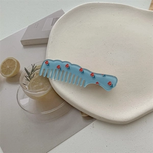 Close-up of light blue wave-shaped floral hair comb with red flower patterns on ceramic tray