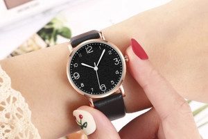 Close-up of minimalist black leather watch with rose gold case on woman's wrist