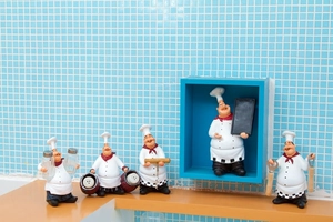 Detailed view of vintage chef resin figurines holding kitchen tools on a wooden shelf