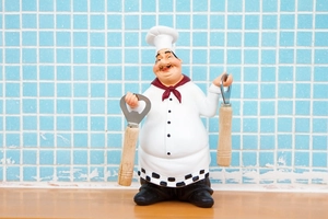 Close-up of chef figurine holding metal bottle openers with wooden handles on wooden base