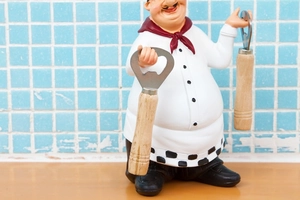 Close-up of vintage chef figurine holding functional metal bottle openers with wood handles