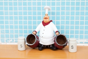 Detail of chef resin figurine holding two white ceramic salt shakers on wooden table