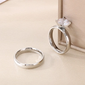 Close-up of a silver couple ring set featuring a 6-prong diamond ring and a polished band