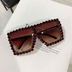 Close-up of oversized square sunglasses with red gradient lenses and rhinestone-encrusted frame