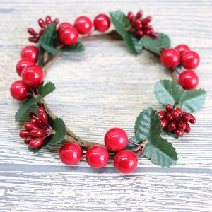 Detailed close-up of Christmas candle ring with red berries, green leaves and rattan base