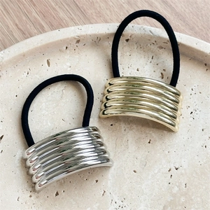 Elegant gold and silver geometric hair ties with striped metal accents on a stone tray