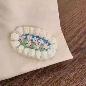Detail of handmade oval embroidery hair clip featuring a pink flower on blue background