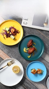 Close-up of matte ceramic dinner plates in yellow, green, and blue on wood table