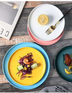 Flat lay of colorful matte ceramic plates with lemon, salad, and wings on wood surface
