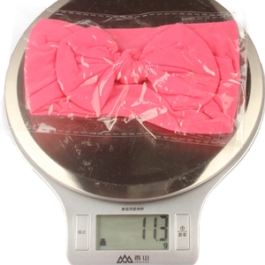 Detailed close-up showing a pink nylon baby headband bow weighing 11.3g on a scale