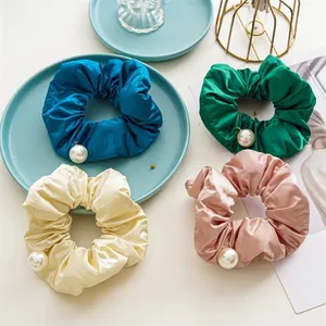 Detail of four colorful satin scrunchies featuring glossy texture and white pearl pendants