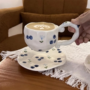 Close-up of ceramic coffee cup with hand-painted blueberry pattern and wavy handle