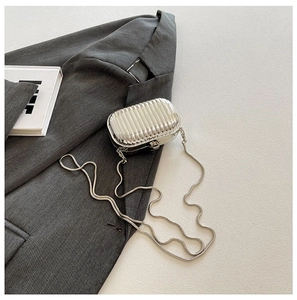 Silver mini suitcase style acrylic crossbody bag with metal chain on a textured background