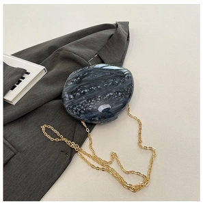 Detail of round marble pattern acrylic evening bag with gold metal chain on a suit jacket