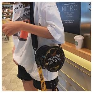 Detail of round black glossy crossbody bag with yellow printed strap in a cafe setting