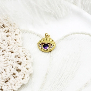 Close-up of golden evil eye pendant with purple gemstone and white zircon accents