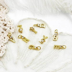 18k gold plated copper letter charms with zircon inlay on a white lace and feather background