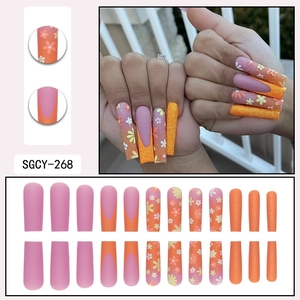Long trapezoid press-on nails featuring orange French tips and floral glitter designs