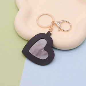 Macro detail of black PU leather heart keychain with mirror and gold metal ring on tray