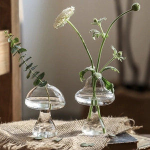 Detail of mushroom-shaped clear glass vases with plants on a rustic linen cloth